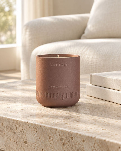 Staging concept based on Caftari’s Scent of Nirvana candle: engraved mauve-brown vessel on travertine beside ivory books