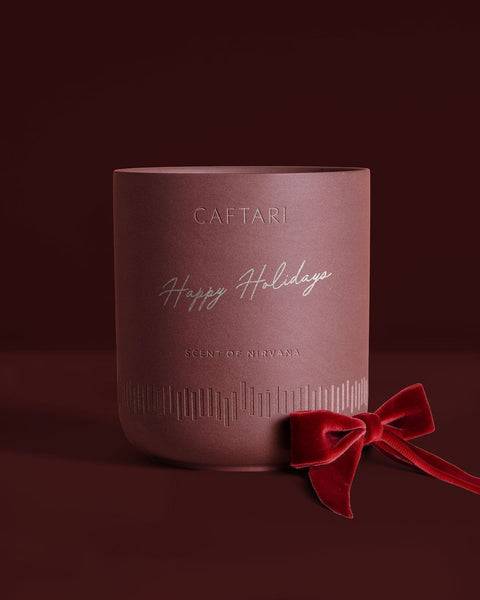 Caftari Scent of Nirvana candle with Happy Holidays engraving and a red ribbon